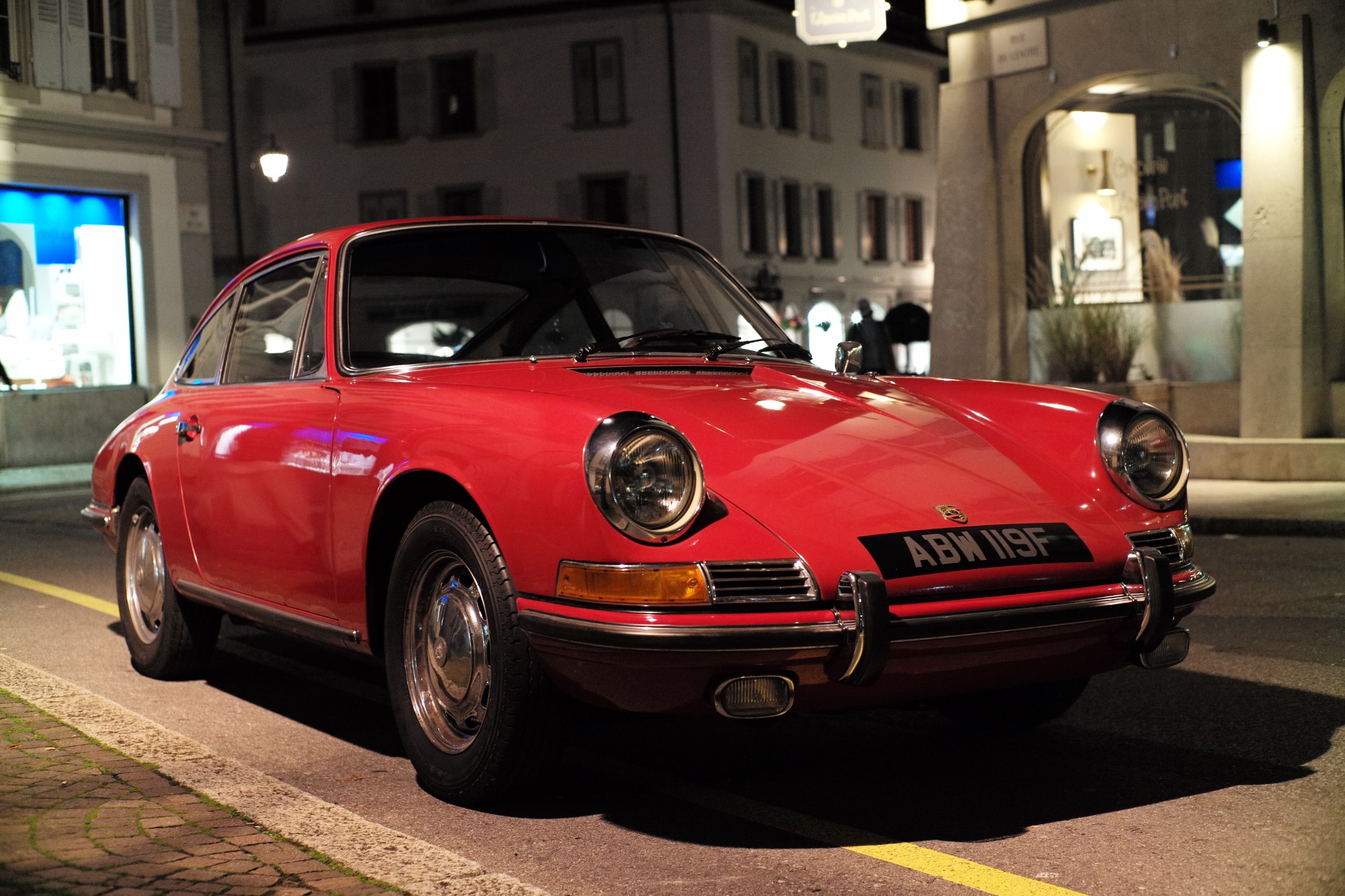 An early chrome-bumper Porsche 911 in red, parked on a street at night